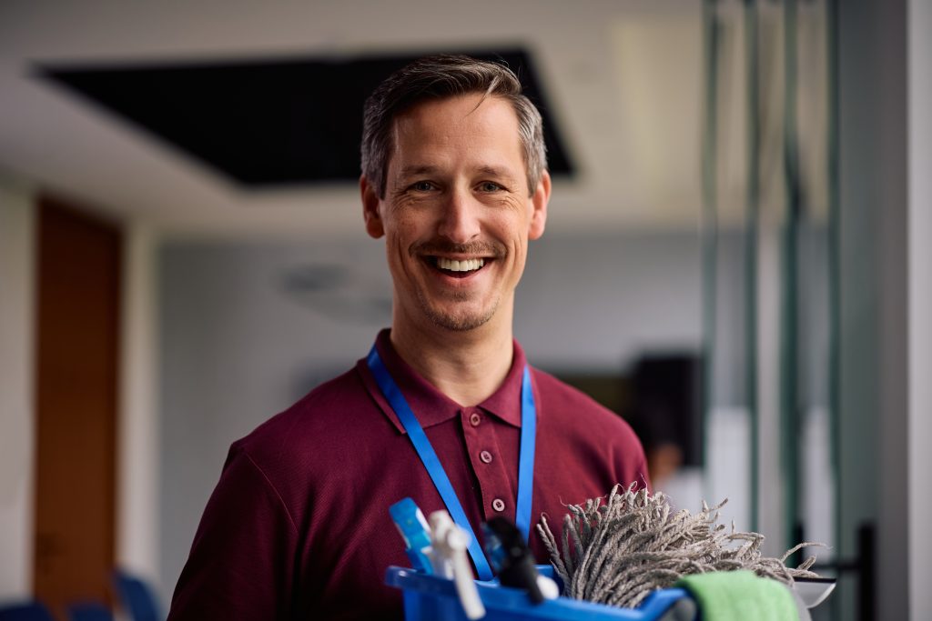 A commercial cleaning professional smiling while holding cleaning supplies while providing office cleaning services.