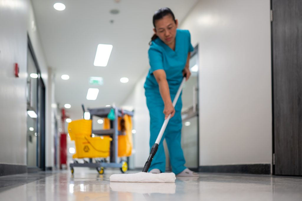A woman in blue scrubs mopping a floor in a hospital.