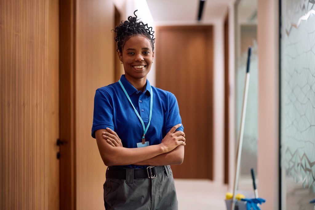 A professional janitorial service provider smiles while cleaning an office hallway,